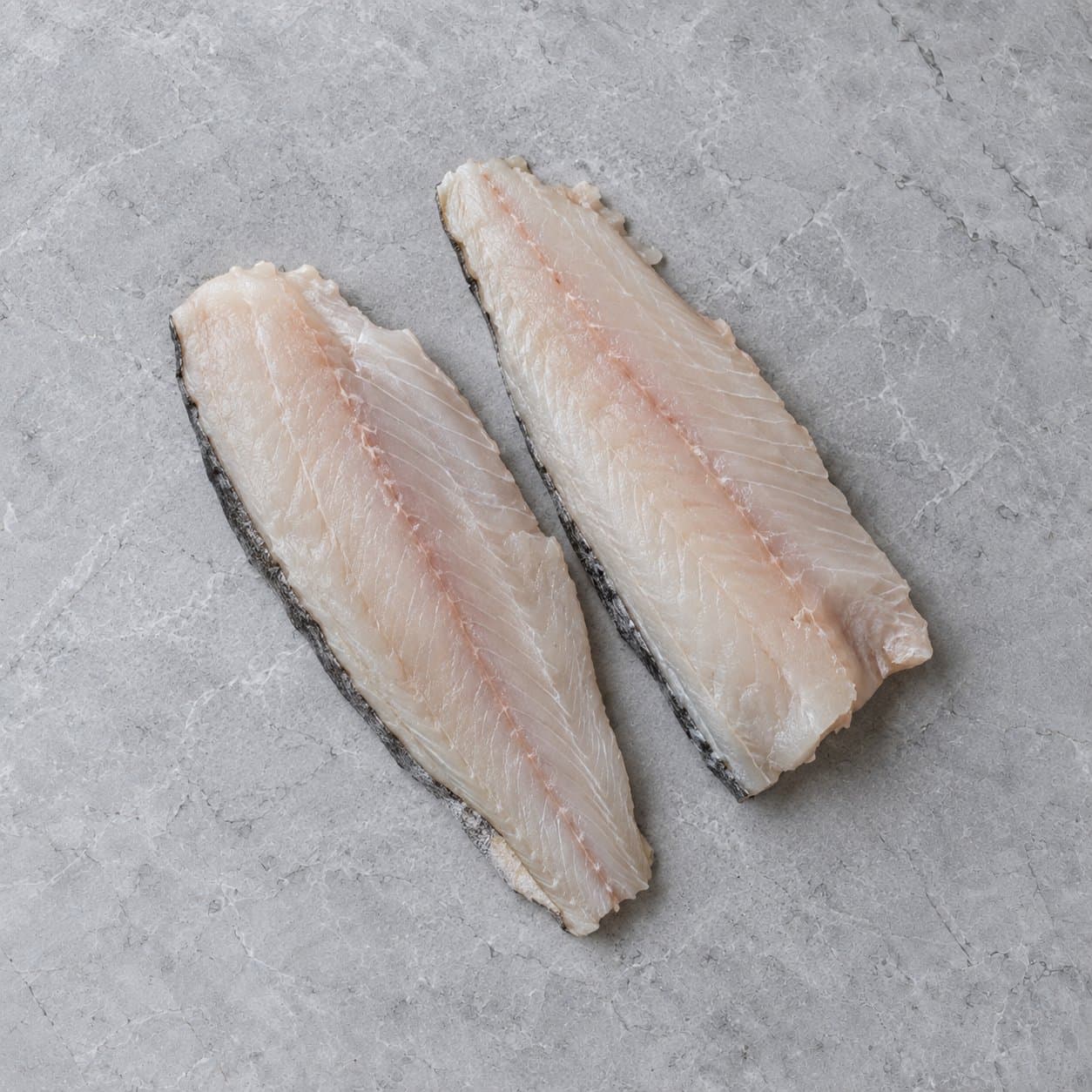 Two raw haddock fillets on grey stone